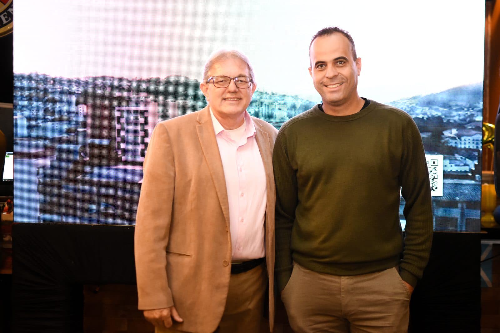 Dois participantes posando diante de painel com vista da cidade