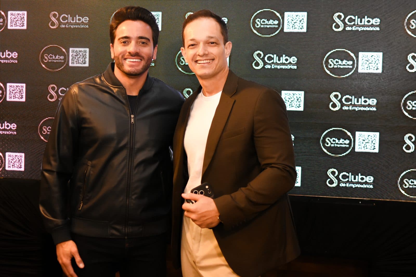 Dois participantes posando diante do painel do Clube de Empresários