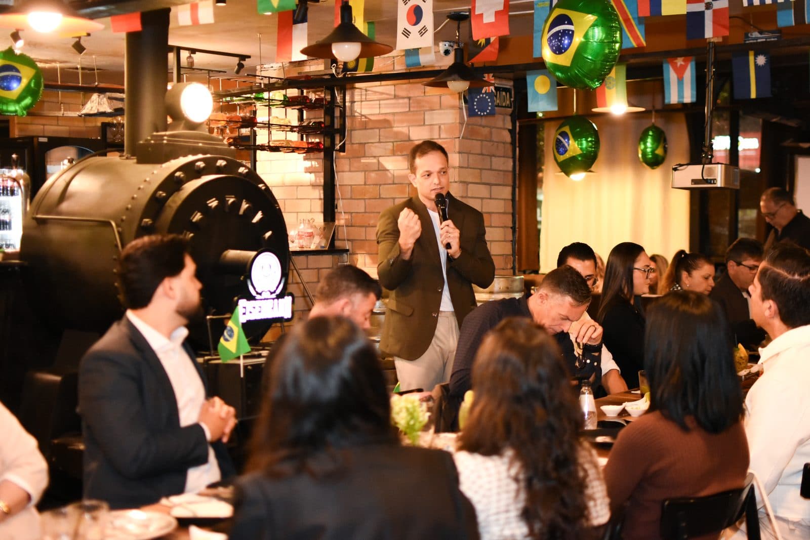 Palestrante falando para plateia em restaurante com bandeiras