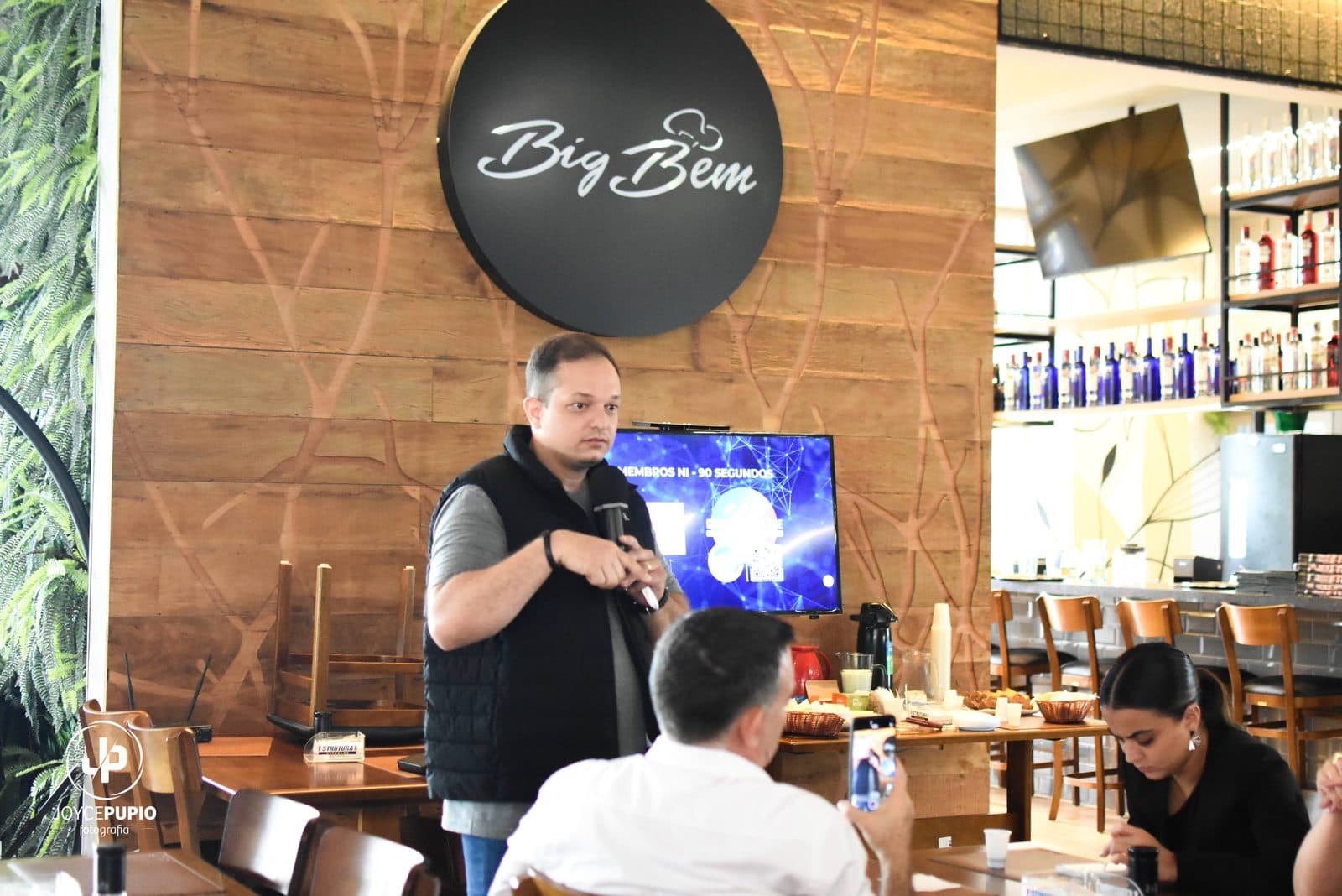 Palestrante com microfone apresentando para mesas em restaurante